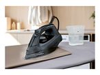 Black steam iron on an ironing board with a measuring cup of water nearby.