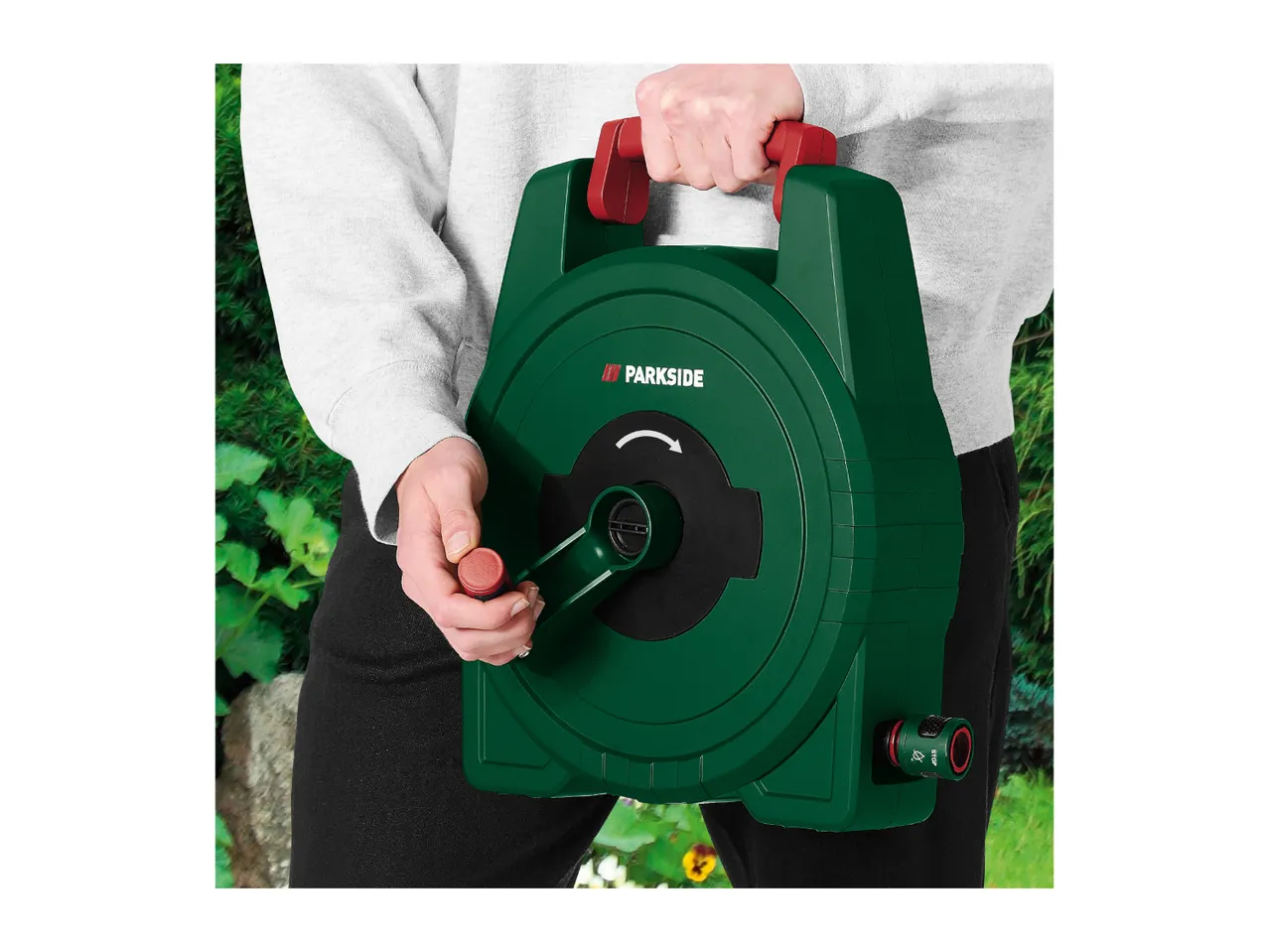 Person holding a green hose reel with red handle and crank, ready for gardening.