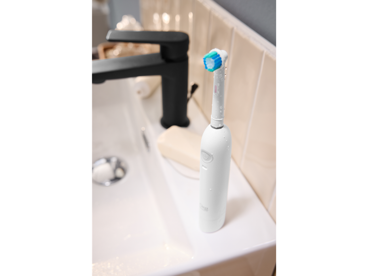 White electric toothbrush with blue bristles on a bathroom sink next to a black faucet.
