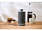 Um moedor de café SilverCrest em uma bancada de cozinha ao lado de uma prensa francesa e uma xícara de café.