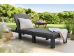 Livarno Wicker Sun Lounger with grey cushions and white pillow on a patio with garden background.