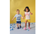 Two kids, a boy in a blue shark T-shirt and a girl in a white rainbow T-shirt, holding hands.