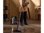 Person cleaning a workshop floor with a wet and dry vacuum cleaner, surrounded by tools.