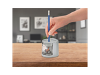 A hand inserts a blue pencil into a grey electric pencil sharpener on a wooden table.