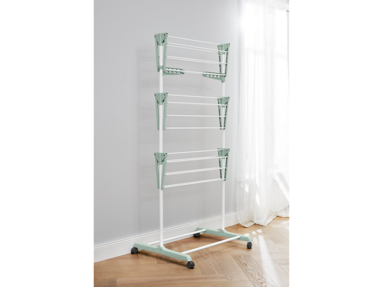 A freestanding, multi-tiered laundry drying rack with light green accents stands on a light wood floor.