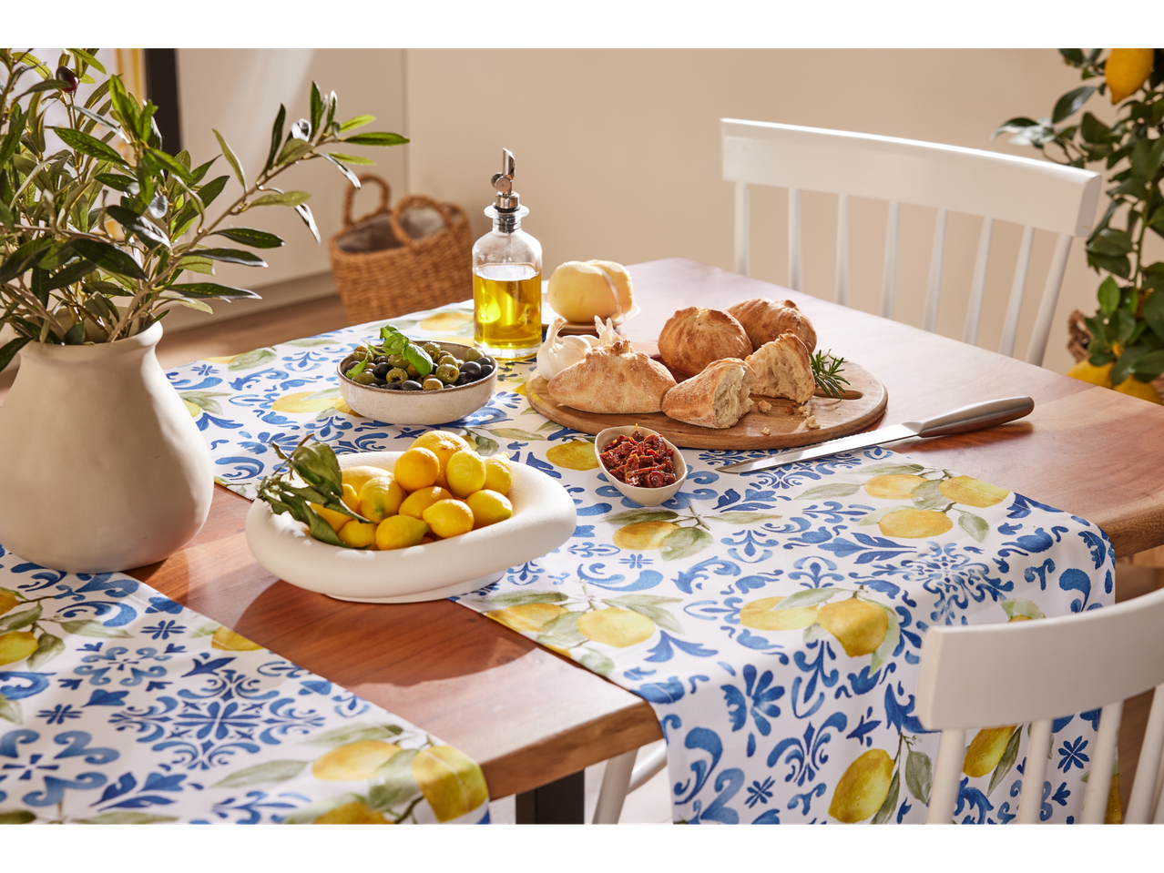 A lemon-themed table runner and placemats adorn a wooden table set for a Mediterranean-style meal.