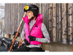 Woman in Esmara® ski base layer and pink vest, smiling by a wooden wall.