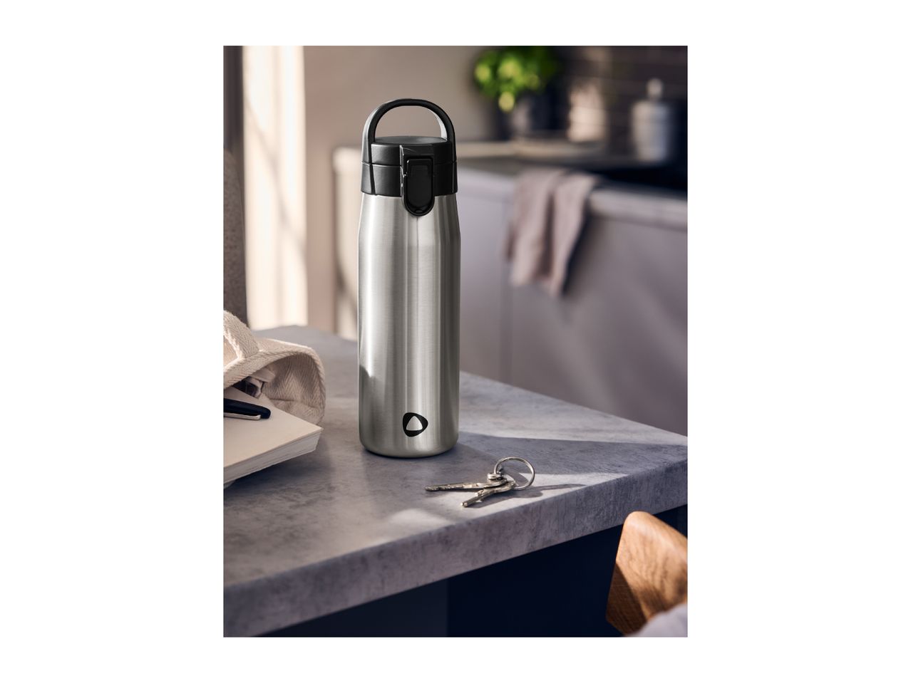 Stainless steel water bottle on a kitchen counter next to keys and a notebook.