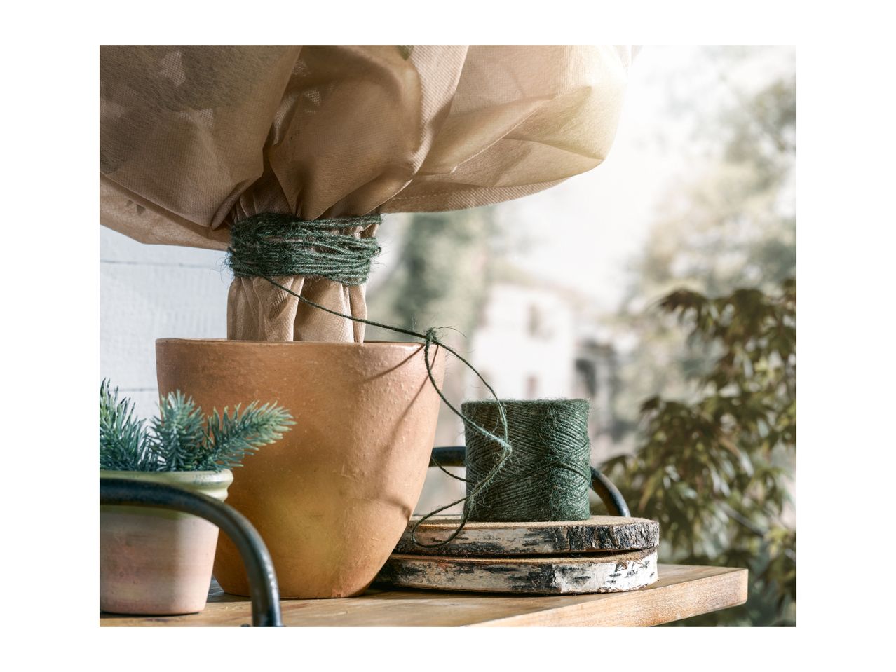 A terracotta pot wrapped in burlap and tied with green twine next to a spool of string.