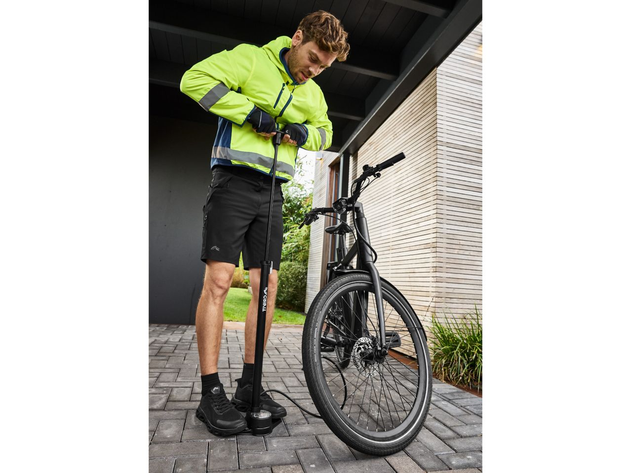 Man in a high-visibility jacket and cycling shorts pumping up a bicycle tire.