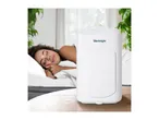 A white dehumidifier on a wooden table with a sleeping woman in the background.