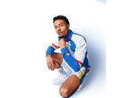 Man in white, blue, red, and yellow athletic jacket and shorts, with matching socks and white sneakers.