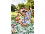 A family enjoys a picnic on a tropical-themed blanket, with children playing and adults relaxing nearby.