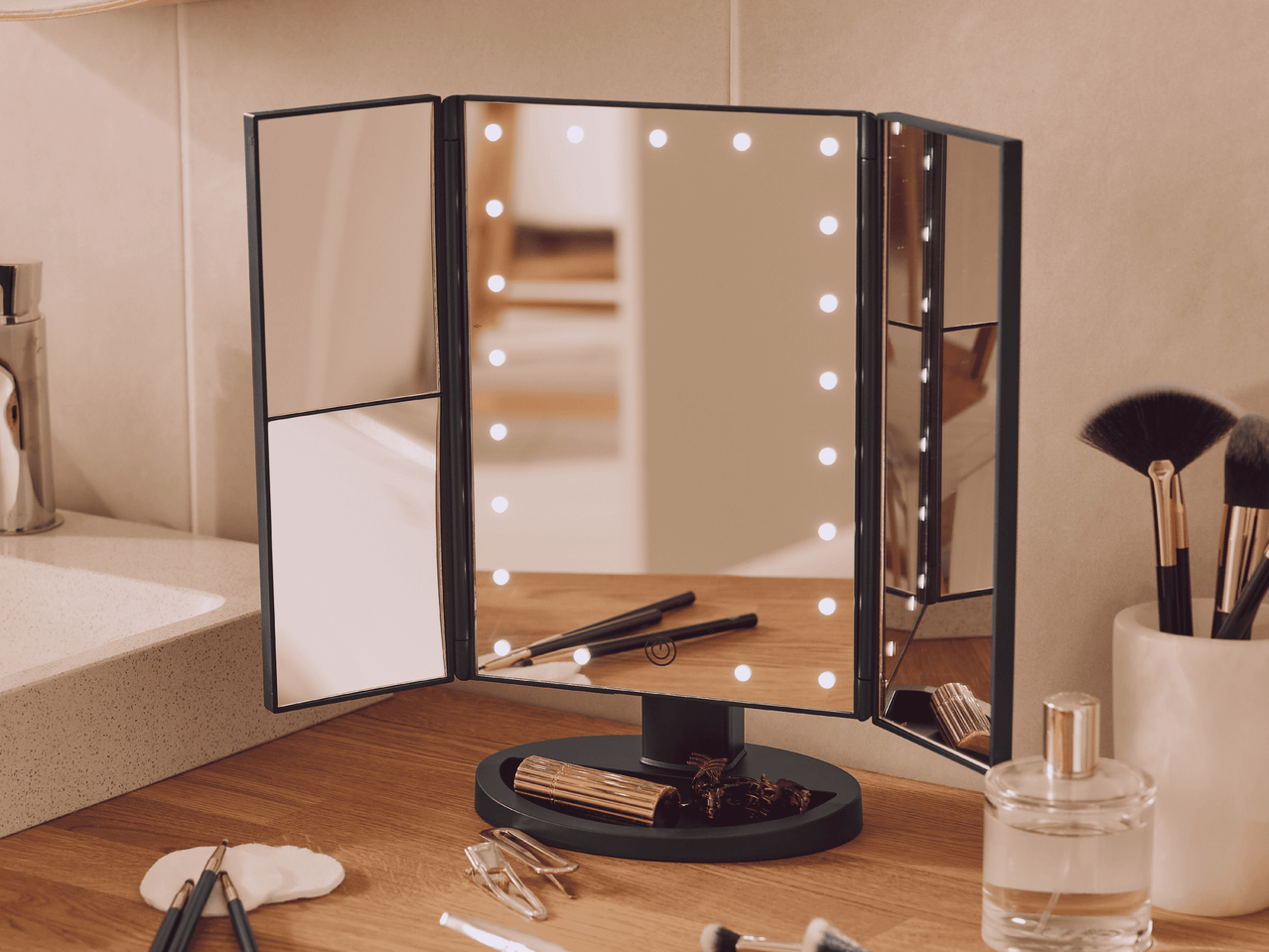 Beleuchteter Kosmetikspiegel mit Make-up-Pinseln und Parfüm auf einem Holztisch.