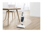 A Bosch cordless stick vacuum cleaner cleans a light wood floor in a modern room.