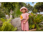 Little girl in a pink dress and hat holding a bird of paradise flower in a garden.