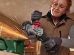 A woman uses a Parkside cordless angle grinder to cut a metal pipe in a workshop.