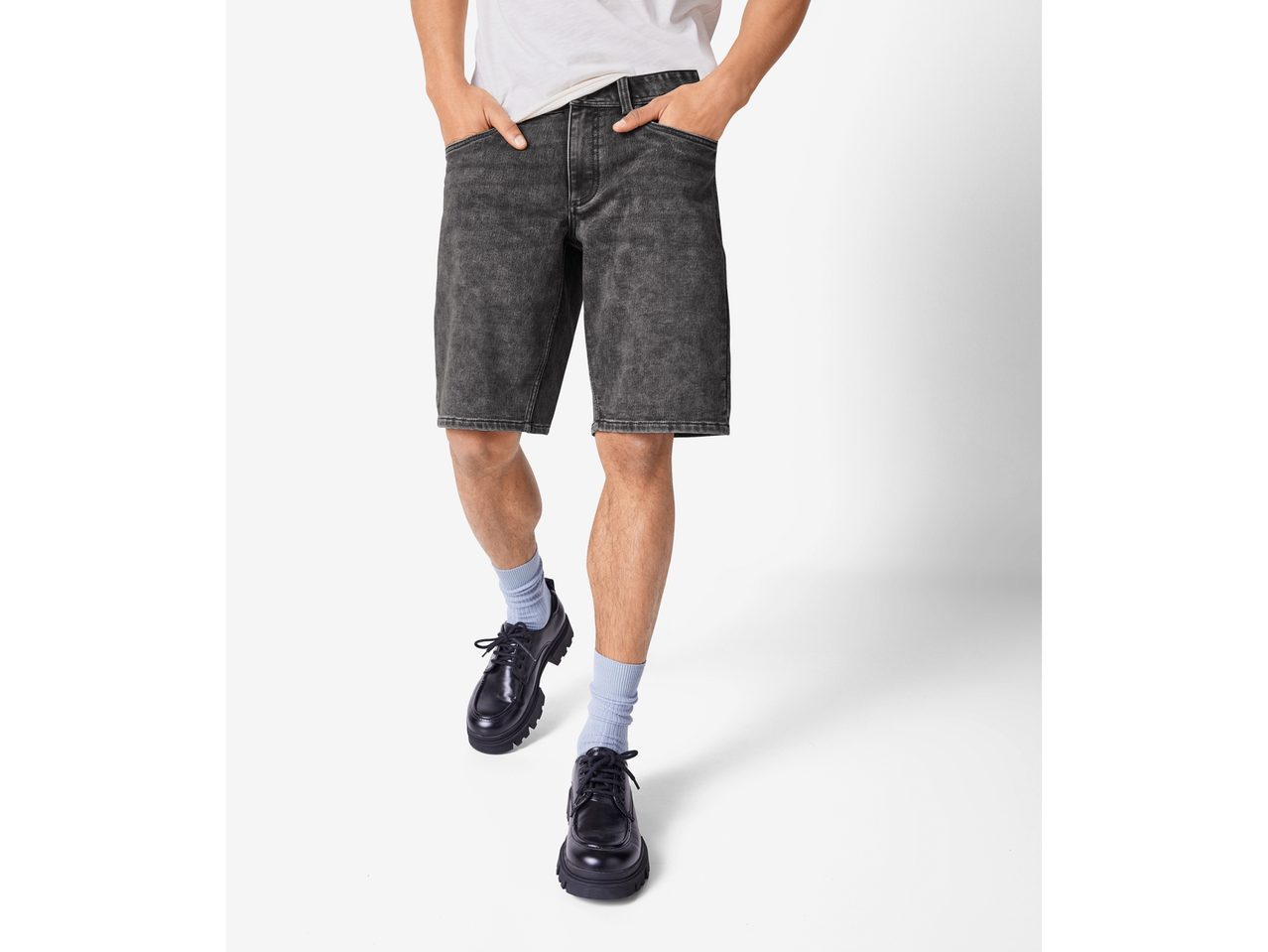 Un bărbat poartă pantaloni scurți din denim negru și pantofi negri.