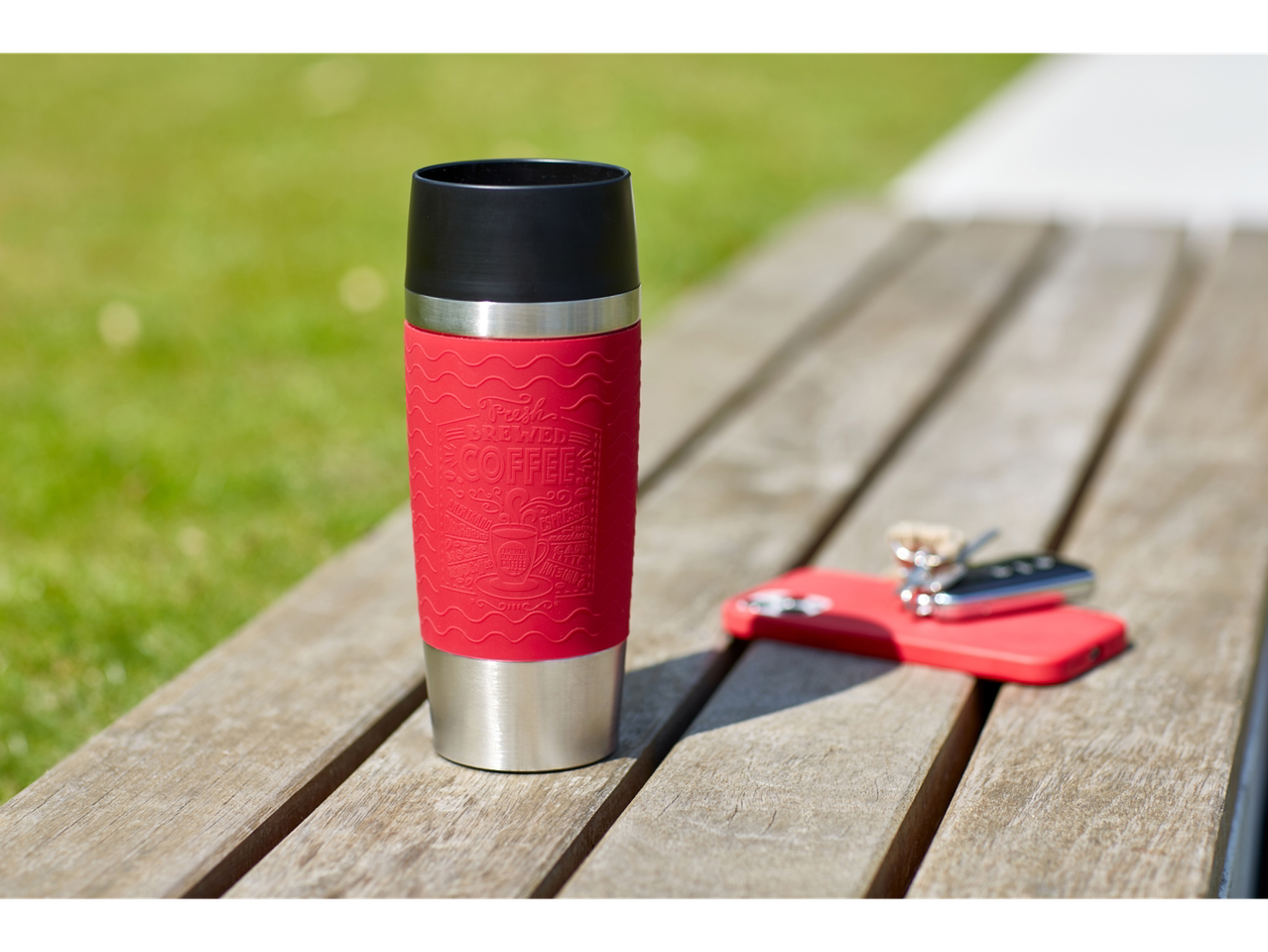 Red Tefal travel mug on a wooden bench with keys and a phone
