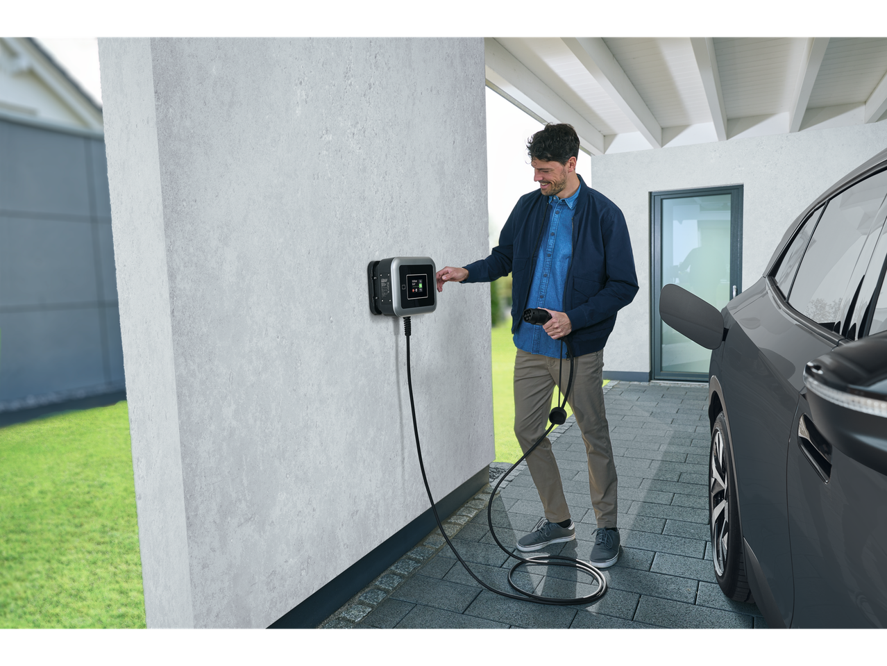 Vyras krauna savo elektromobilį namų įkrovimo stotelėje