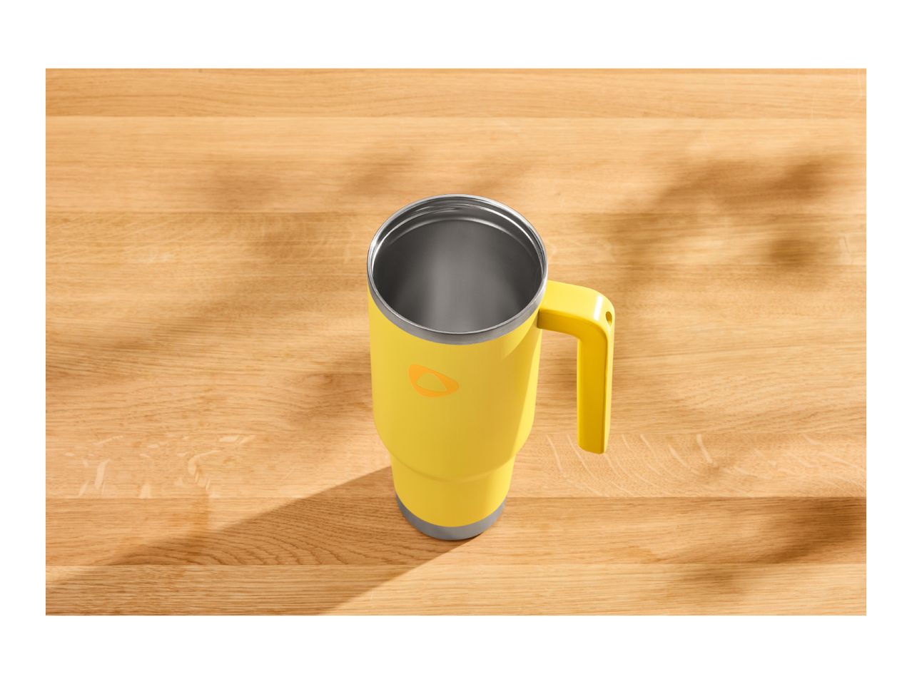 Yellow travel mug with a handle on a wooden table with shadows.