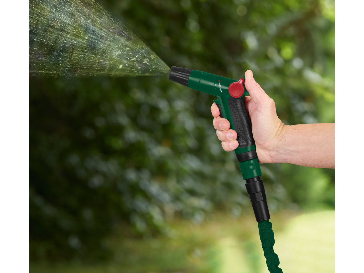 Χέρι κρατάει ένα εύκαμπτο λάστιχο κήπου PARKSIDE που ψεκάζει νερό.