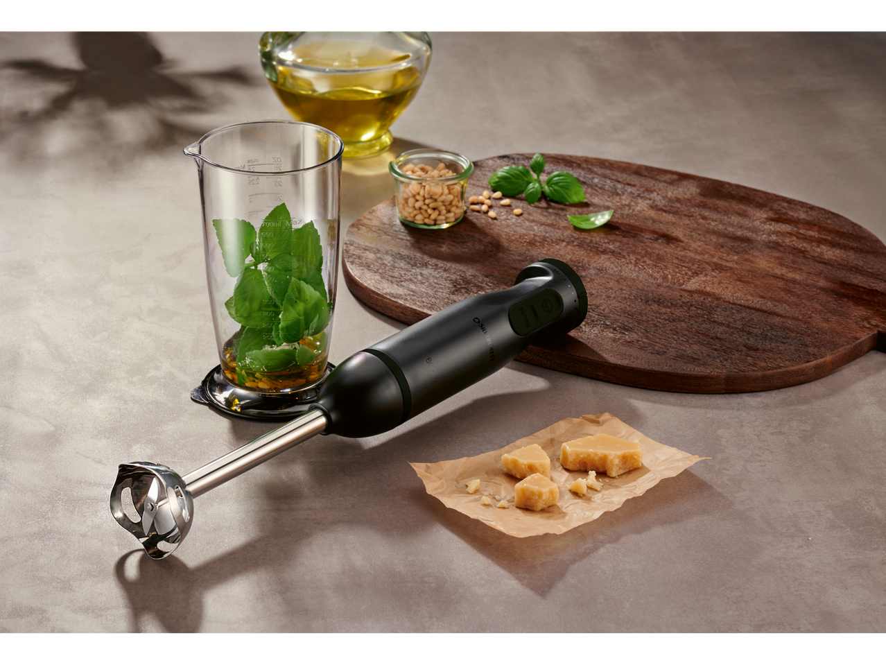 A SILVERCREST® hand blender set with ingredients for pesto, including basil, pine nuts, olive oil, and Parmesan cheese.