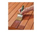 Hand applying wood stain to a wooden surface with a paintbrush.