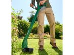 A person uses a Greenworks string trimmer to cut grass.
