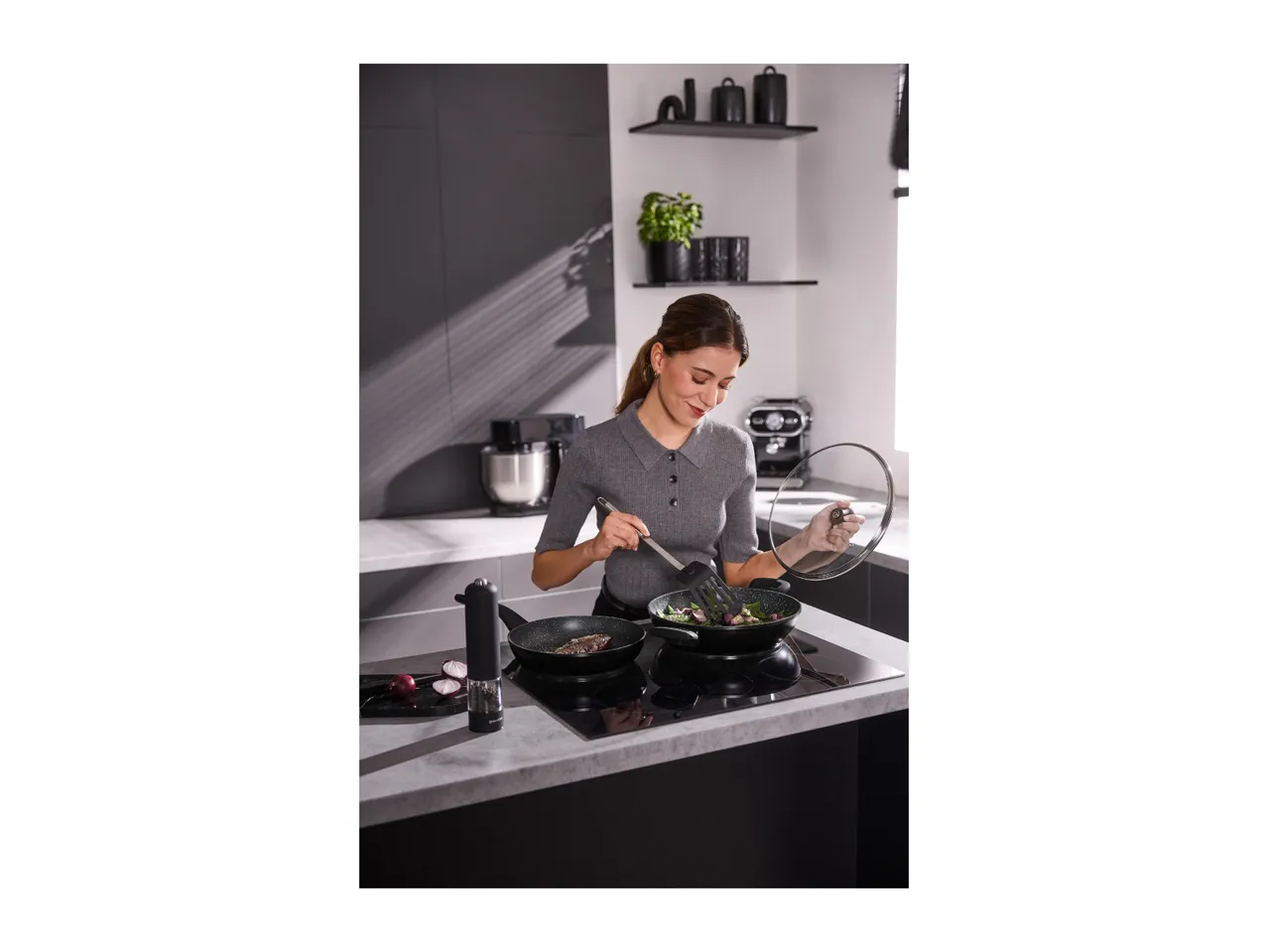 Woman cooking with two frying pans on an induction hob in a modern kitchen.