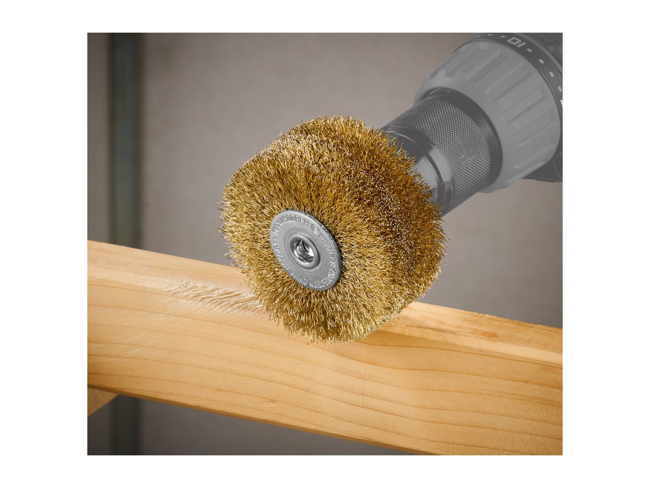 Wire brush attachment on a drill, brushing a wooden plank.