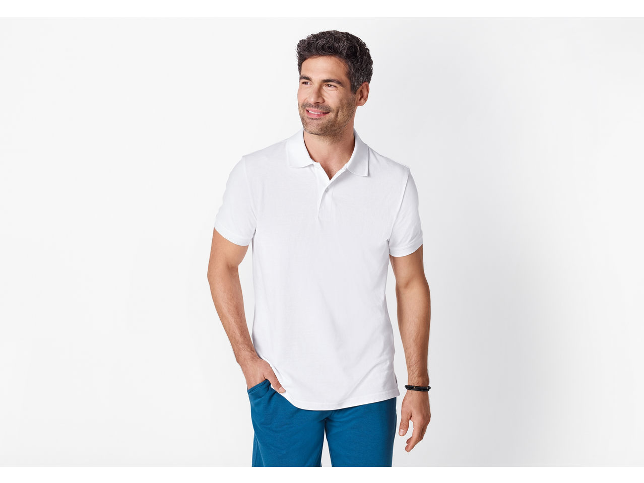 Nasmiješeni muškarac u bijeloj polo majici i plavim kratkim hlačama, s rukom u džepu.