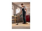 Man in overalls vacuuming sawdust from the floor in a workshop.