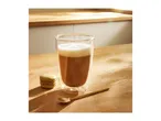 Latte in a double-walled glass with a green macaron and gold spoon on a wooden table.