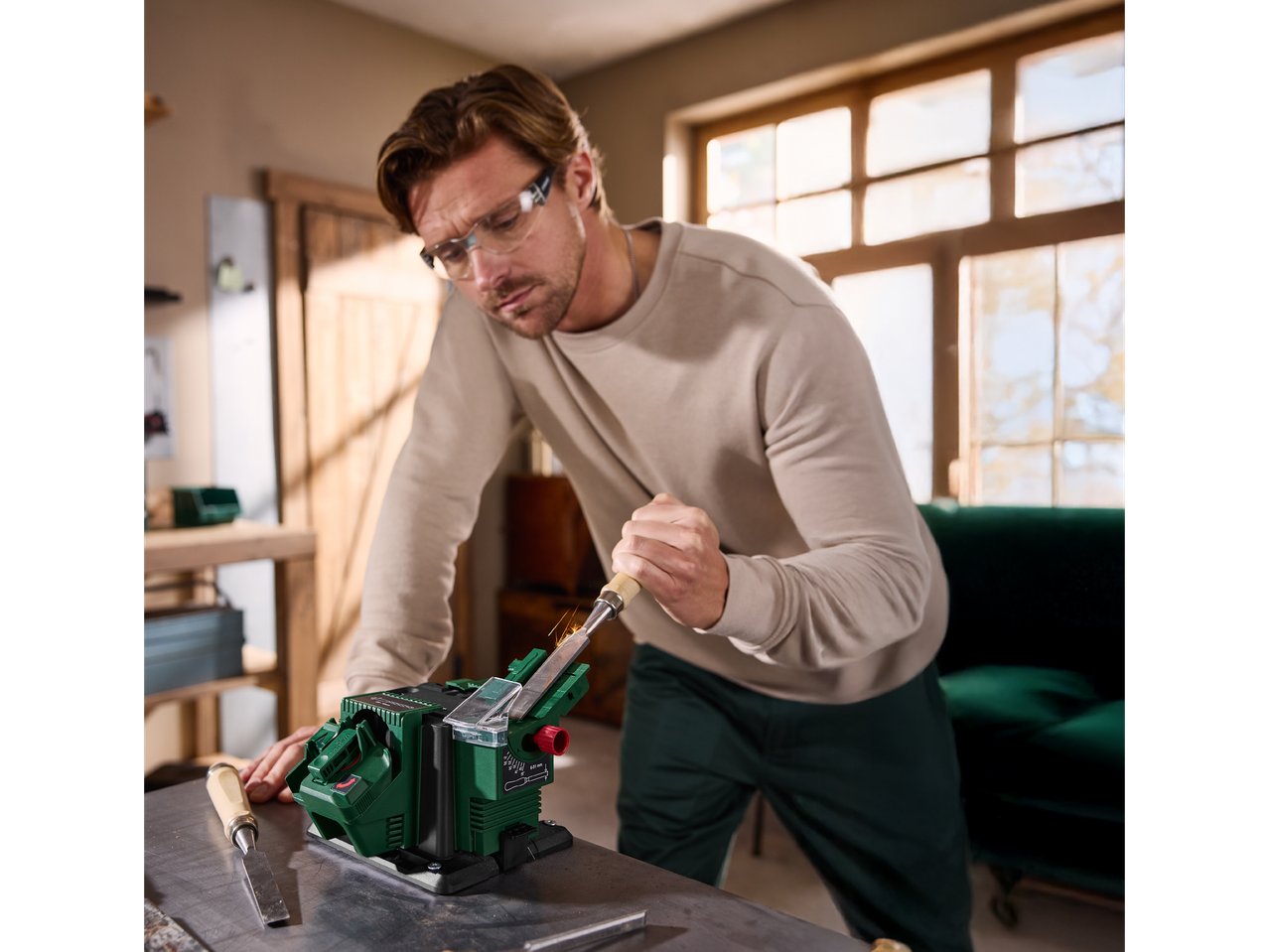 Мъж използва електрическа машина за заточване на длето, искри летят.