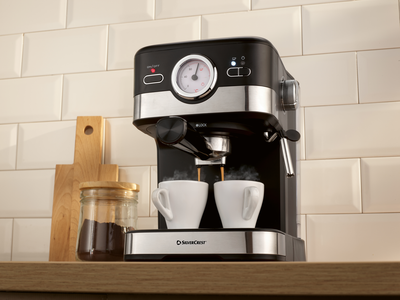 Espressor negru și argintiu preparând două cești de cafea într-o bucătărie.