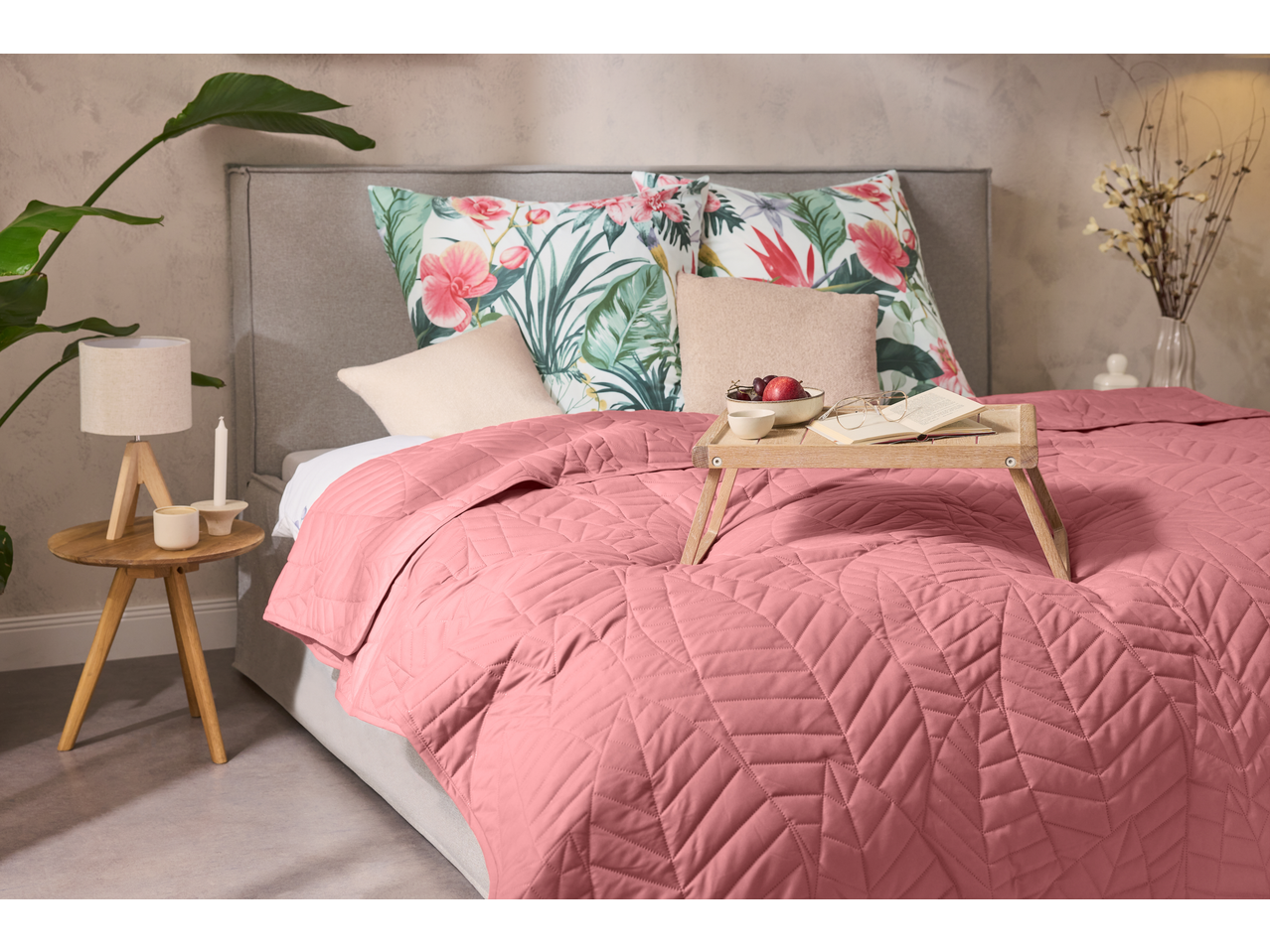 Cuvertură roz LIVARNO cu model geometric pe un pat cu perne florale.