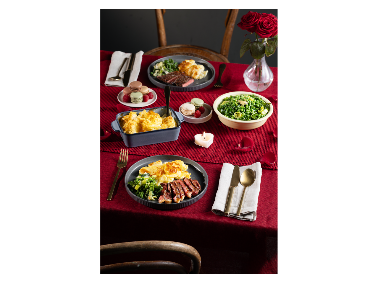 A romantic dinner with steak, potato gratin, green vegetables, macarons, and red roses.