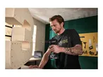 Man drilling into a wooden shelf with a cordless drill, surrounded by various tools.