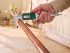 A person using a Parkside digital caliper to measure the diameter of a copper pipe.