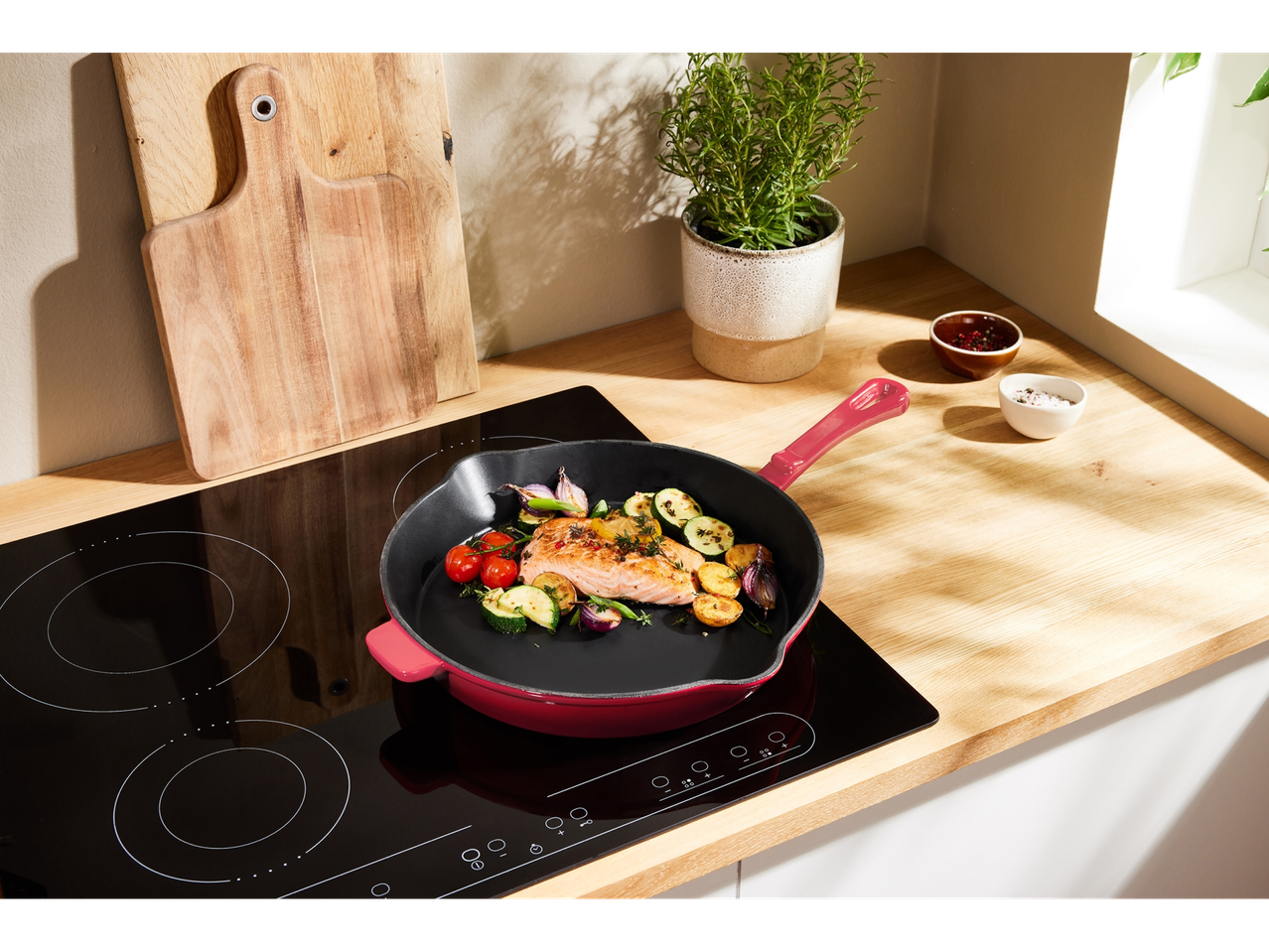 Un piatto di salmone e verdure che cuoce in una padella in ghisa rossa su un piano cottura a induzione nero.