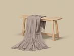 A soft, light brown blanket draped over a wooden bench on a neutral background.