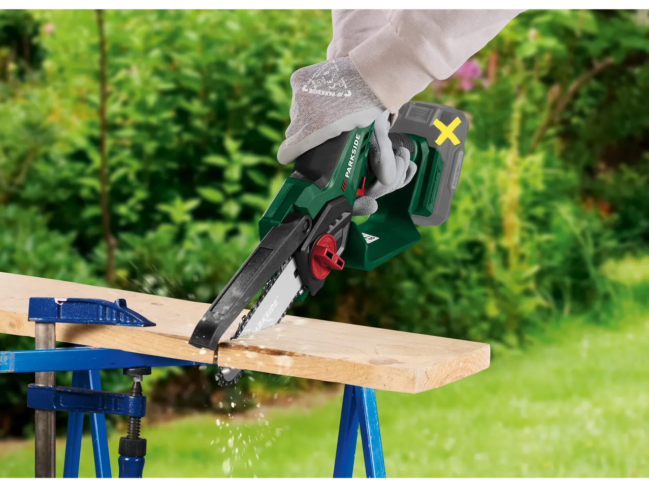 Cordless chainsaw cutting a wooden board in a garden.