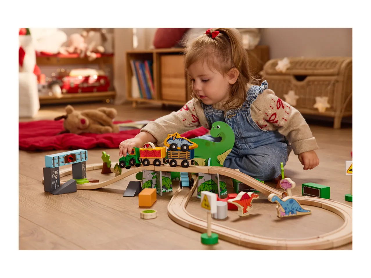 Toddler playing with a wooden dinosaur-themed train set on the floor.