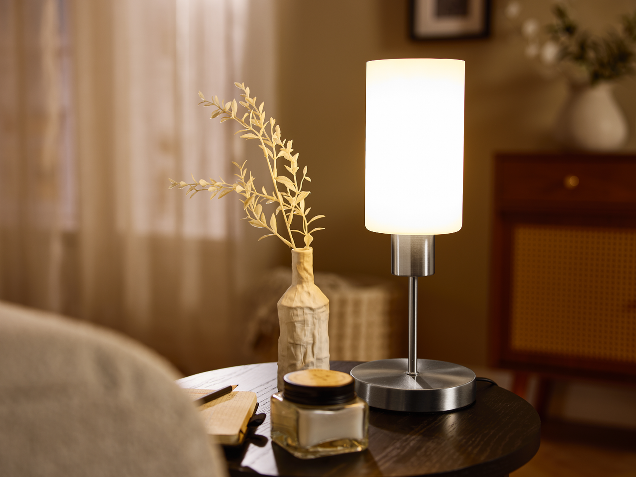 Настолна лампа с бял абажур и ваза със сухи цветя на дървена маса