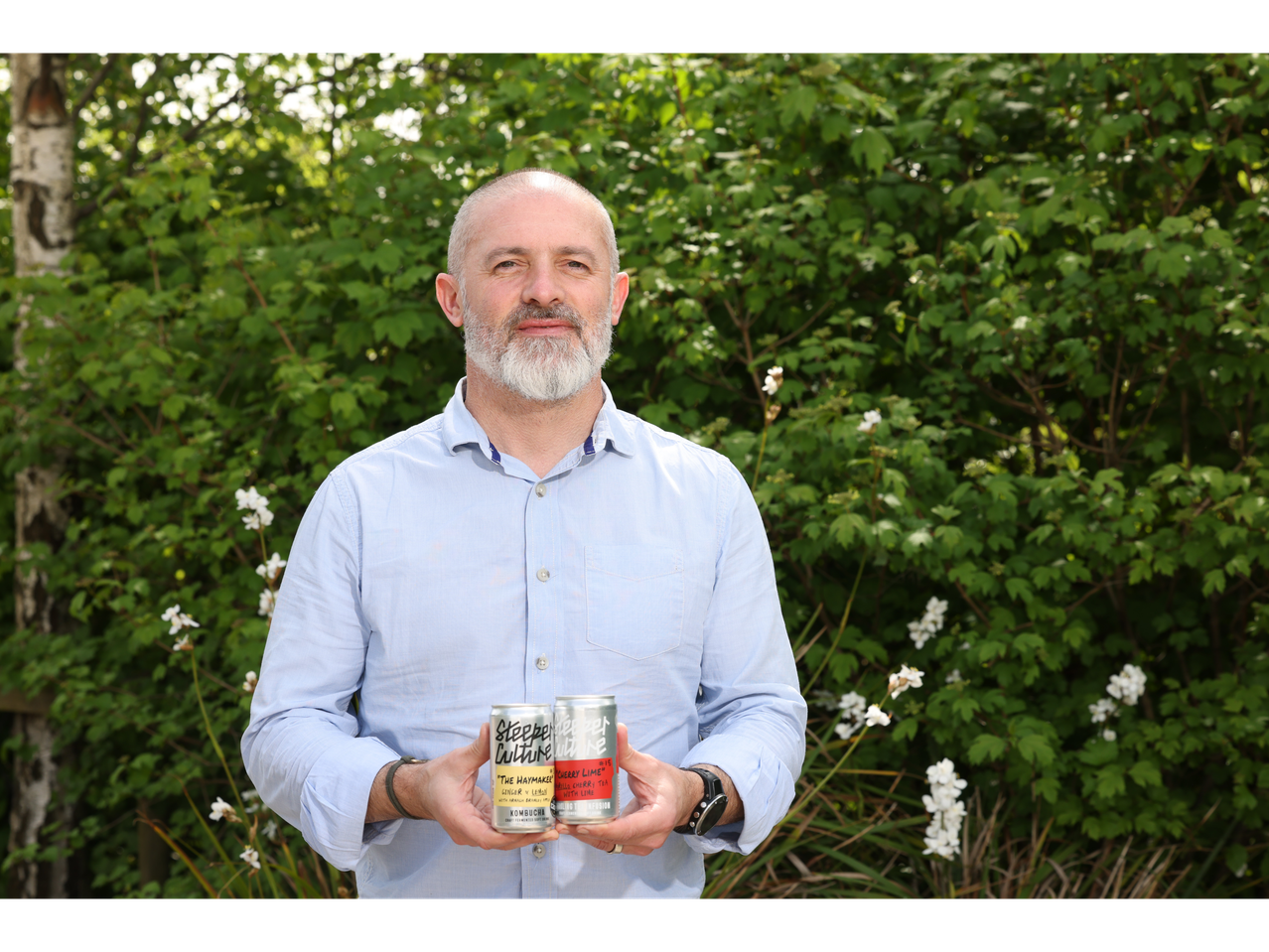 Man holding two cans of Steeper Culture kombucha, one ginger & lemon and one cherry lime.
