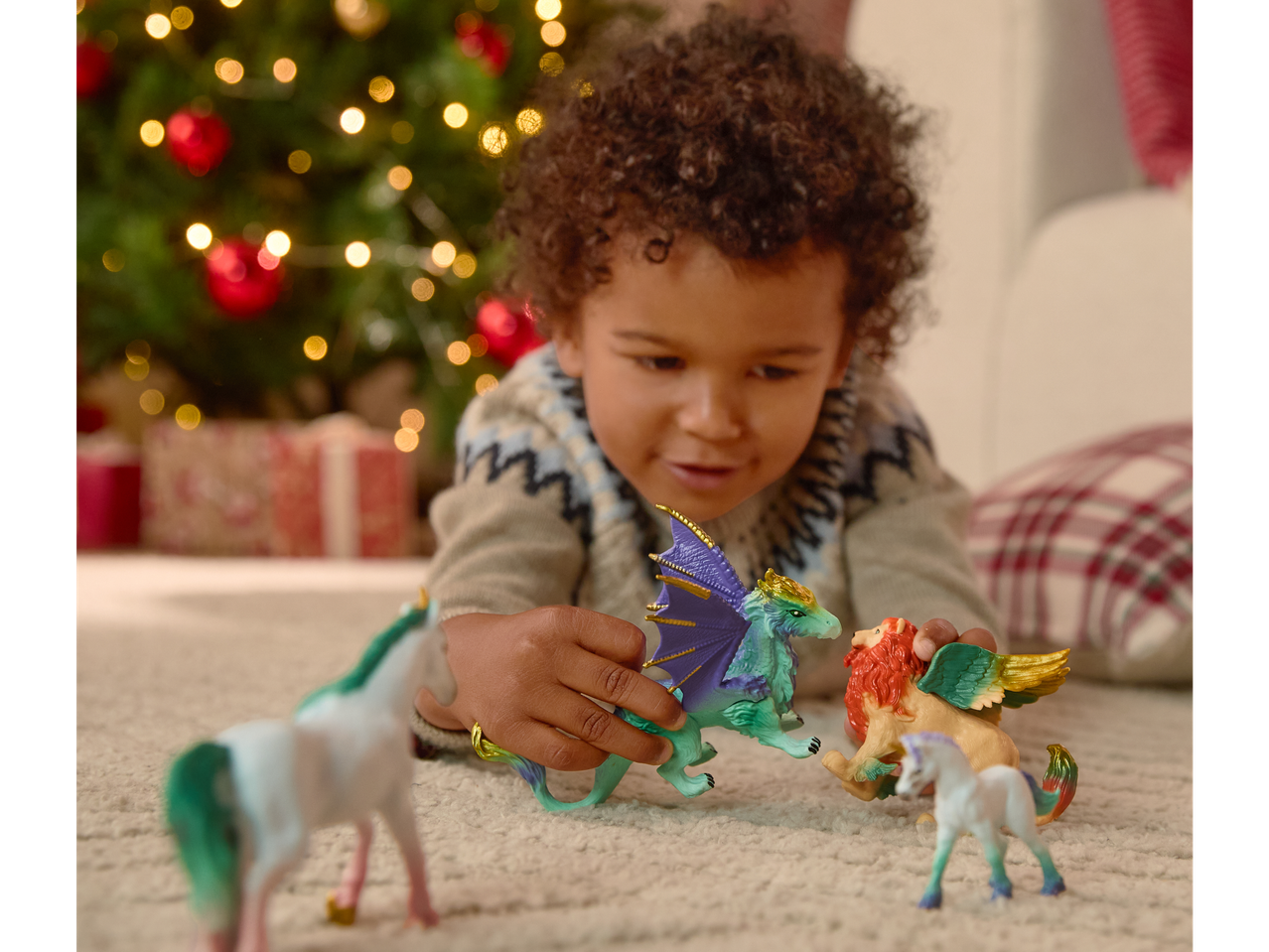 Copil care se joacă cu figurine de animale LUPILU® în fața unui brad de Crăciun.