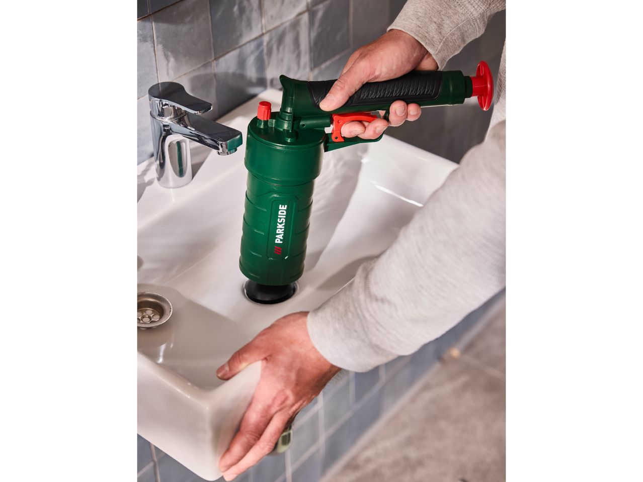 A person using a green drain blaster to clear a sink in a bathroom.