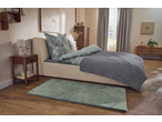 Bedroom with a bed featuring patterned duvet covers, a grey quilted throw, and a green rug.