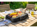 Grill elétrica SilverCrest com legumes, frango e abacaxi grelhados em uma mesa de madeira ao ar livre.